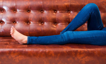 女人腿穿牛仔裤放松电影剧院首页棕色（的）皮革沙发放松假期概念床上时间睡觉概念人生活方式假期特写镜头女孩脚