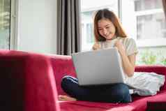 年轻的女人冲浪互联网移动PC红色的沙发很高兴成功的交易房子销售在线购物概念商人市场营销概念幸福交易员主题