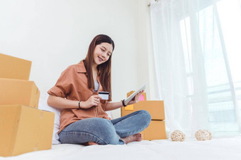美亚洲女人平板电脑信贷卡开始小业务企业家锻造检查订单列表卧室年轻的快乐自由女人购物在线市场营销发送包裹