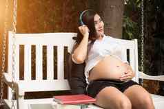 亚洲年轻的怀孕了女人放松听音乐摇摆不定的公园花园书人娱乐概念幸福快乐概念单妈妈寡妇主题