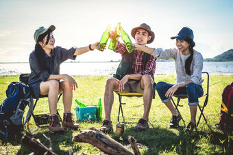 集团年轻的亚洲朋友享受野餐聚会，派对湖野营背包椅子年轻的人敬酒欢呼瓶啤酒人生活方式概念户外背景主题