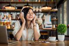 快乐亚洲女人放松听音乐咖啡商店电脑移动PC咖啡杯人生活方式概念自由在户外工作场所在户外主题