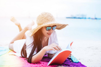 美亚洲女人假期海滩女孩穿翼他阅读书色彩斑斓的席海生活方式快乐生活概念旅行假期主题
