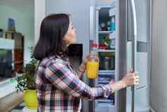 女人打开冰箱首页厨房持有瓶橙色汁