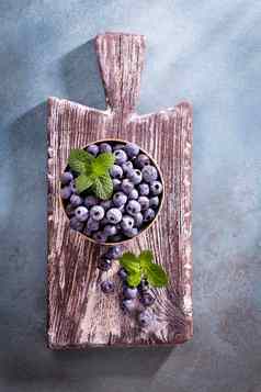 碗新鲜的蓝莓乡村木董事会有机食物蓝莓薄荷叶健康的生活方式