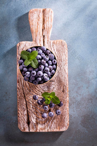 碗新鲜的蓝莓乡村木董事会有机食物蓝莓薄荷叶健康的生活方式