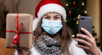 圣诞节在线年轻的女孩圣诞老人老人他医疗面具会谈智能手机视频调用朋友父母圣诞节冠状病毒