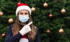 关闭肖像女人穿圣诞老人老人他医疗面具情感显示手指背景圣诞节树冠状病毒流感大流行