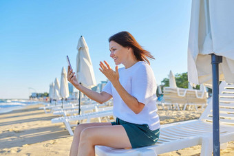 快乐中年女人会说话的智能手机视频调用海滩