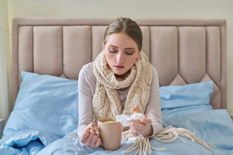 生病的年轻的女人坐着首页床上热杯茶手帕