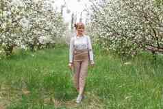 美丽的年轻的金发女郎女人白色衬衫背包摆姿势苹果树开花春天花园