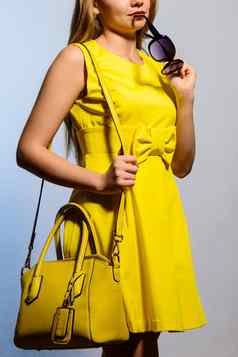 时尚年轻的女人黄色的衣服手提包太阳镜
