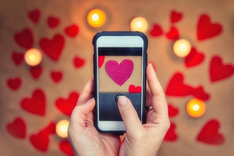 女手持有移动电话采取照片粉红色的浪漫的情人节心问候卡情人节一天前视图浪漫的背景