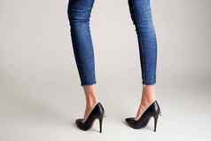 女人牛仔裤黑色的高非常鞋子挂锁摆姿势灰色的背景
