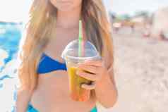 年轻的女孩少年持有喝彩色的冷不含酒精的鸡尾酒手背景海海滩