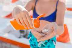 年轻的女孩持有防晒霜手弄脏的保护太阳背景海海滩