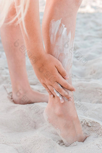 年轻的女孩的手<strong>涂片</strong>防晒霜腿海滩沙子