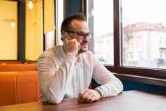 年轻的有吸引力的商人白色衬衫眼镜坐在表格咖啡馆会说话的电话微笑