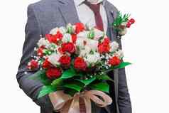 新郎西装持有婚礼花束白色红色的花玫瑰绿色叶子手特写镜头