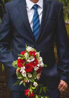 新郎白色衬衫蓝色的西装领带持有婚礼花束新娘白色红色的花玫瑰