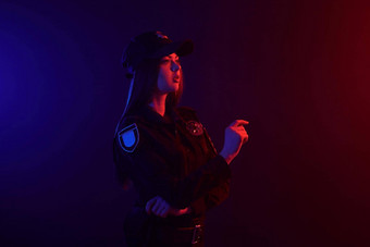 红发的女警察官摆姿势相机黑色的背景红色的蓝色的背光
