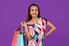 美丽的年轻的女人色彩斑斓的购物袋美妙的紫色的背景