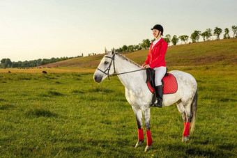 年轻的女人骑手穿红色的大礼服白色马裤马晚上日落光