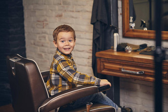 肖像时尚的男孩穿着衬衫牛仔裤理发店坐着椅子理发店工作场所