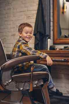 肖像时尚的男孩穿着衬衫牛仔裤理发店坐着椅子理发店工作场所