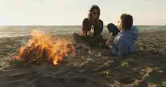 爱的年轻的夫妇坐着海滩篝火喝啤酒