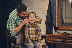 时尚的孩子坐着椅子理发店年轻的父亲背景
