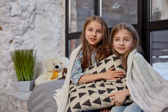 图像可爱的姐妹坐着窗台上覆盖毯子拥抱