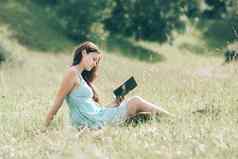 年轻的女学生阅读书坐着草坪上公园