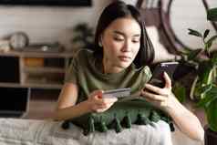 在线购物亚洲女人购买在线购物应用程序移动电话信贷卡信息支付坐着首页生活房间