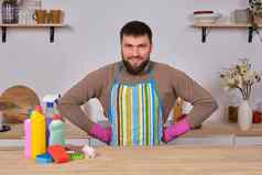 年轻的英俊的有胡子的男人。厨房显示清洁工作人员洗涤剂刷喷雾准备好了真正的清洁持有手臀部