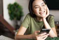 年轻的亚洲女人放置订单等待交付移动电话应用程序坐着首页窗口