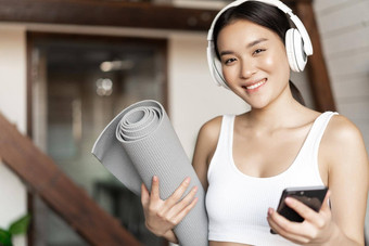 微笑亚洲女孩耳机听音乐首页锻炼地板上席持有移动电话健身练习生活房间