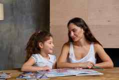 肖像妈妈。帮助小甜蜜的可爱的女儿使家庭作业在室内快乐家庭