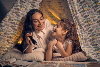 妈妈。女儿坐着超视距雷达帐篷阅读故事手电筒快乐家庭