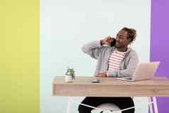 非洲式发型年轻的男人。坐在首页办公室流感大流行电话