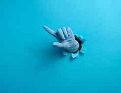 手蓝色的医疗手套坚持撕裂洞蓝色的纸背景指数手指提高了部分身体方向