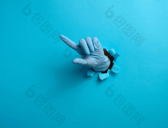 手蓝色的医疗手套坚持撕裂洞蓝色的纸背景指数手指提高了部分身体方向