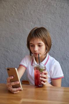 女孩阅读信息电话喝红色的冰冷的鸡尾酒表格咖啡馆