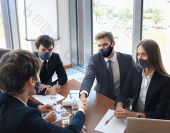 商人预防面具摇晃手密封交易合作伙伴的同事们穿预防面具办公室