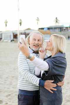 高加索人养老金领取者使自拍智能手机沙子海滩