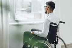 年轻的禁用男人。坐着轮椅窗口