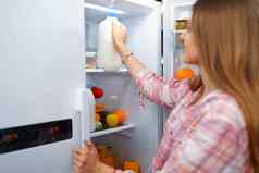肖像年轻的金发女郎女人采取食物冰箱