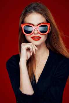 漂亮的女人穿太阳镜时尚摆姿势发型红色的背景