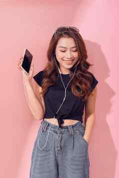图像快乐年轻的美丽的女人摆姿势孤立的粉红色的墙背景听音乐耳机移动电话
