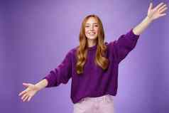 女孩拉伸手横盘整理问候朋友给温暖的拥抱微笑广泛的相机站快乐的想要拥抱紫色的背景穿紫罗兰色的毛衣裤子